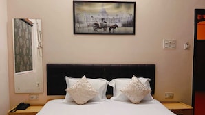 A hotel room with a bed, two pillows, a headboard, a nightstand, a telephone, and a painting on the wall. - Amit Hotel (Kolkata)