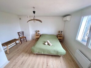 Een slaapkamer met een groen bed, houten meubels, een bankje, een bureau, een lamp en een raam.