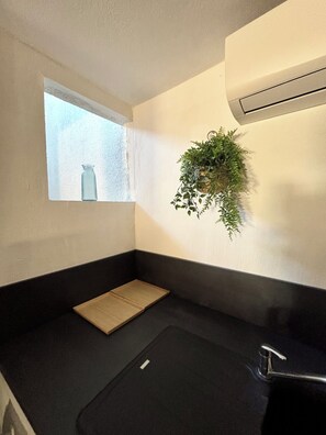 Ein Badezimmer mit Fenster, einer hängenden Pflanze, einem Handtuchhalter und einer Badewanne.
