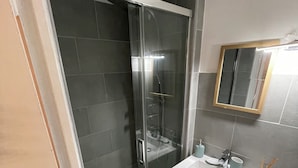 Et badeværelse med en glasafskærmet brusekabine, en hvid vask og et spejl på væggen.