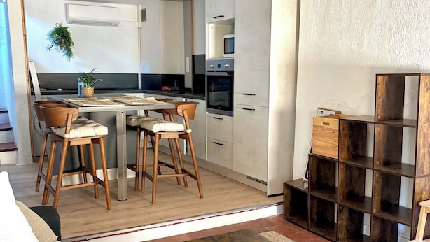 En moderne stue med et træbord, en sofa og et køkkenområde med hvide skabe og en mikrobølgeovn.