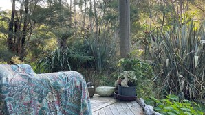 Une terrasse en bois agrémentée d’une couvre-lit à motifs, entourée d’une végétation luxuriante et d’arbres.