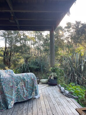 Una terraza de madera con un edredón estampado, rodeada de abundante follaje y árboles.