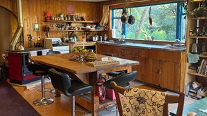 Une cuisine avec des meubles de rangement en bois, une table à manger avec des chaises, une fenêtre ornée de plantes et un extincteur rouge.