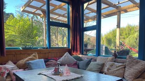 Une pièce chaleureuse avec un banc en bois, une table avec un set de table et une vue sur la verdure grâce à de grandes fenêtres.