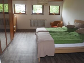 A bedroom with a bed, a chair, a radiator, and windows.