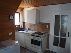 A compact kitchen with a sink, stove, and a clock on the wall.
