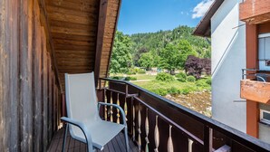A wooden balcony with a chair, overlooking a forested area and a clear sky.