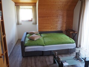Une chambre moderne avec un plafond en bois, un lit avec une literie verte, une table basse en verre et une fenĂȘtre avec des rideaux.
