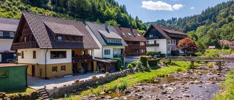 Eine Reihe von traditionellen Chalets mit geneigten Dächern, einem Steinweg und einem Fluss im Vordergrund.