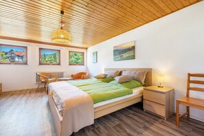 A bedroom with a wooden ceiling, a bed with green bedding, a nightstand with a lamp, a chair, and a view of the outside through a window. - Alte Schmiede by the Stream, Murgleiter & Schwarzwald Plus Card (Baiersbronn)