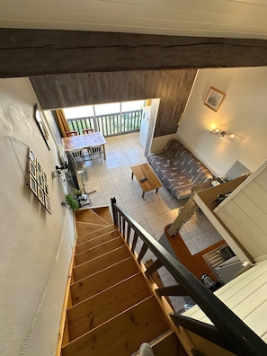 Un escalier menant à un balcon aménagé avec un coin repas, un canapé et un espace cuisine.