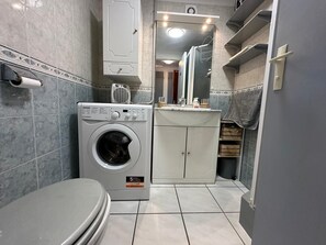 A compact bathroom with a washing machine, toilet, and a small sink area.