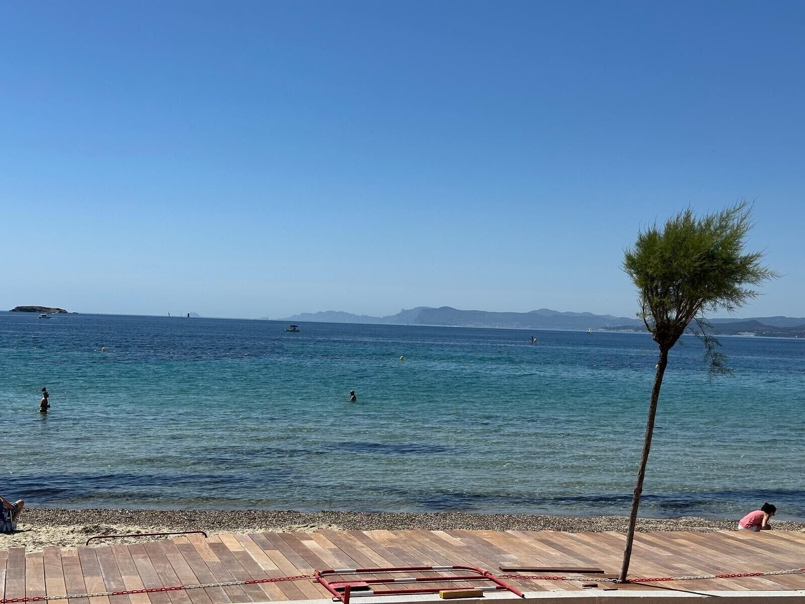 A beach with a wooden deck, a single tree, and calm water.. T2 Apartment 5 Minutes from the Beach with Wi-Fi and Air Conditioning
