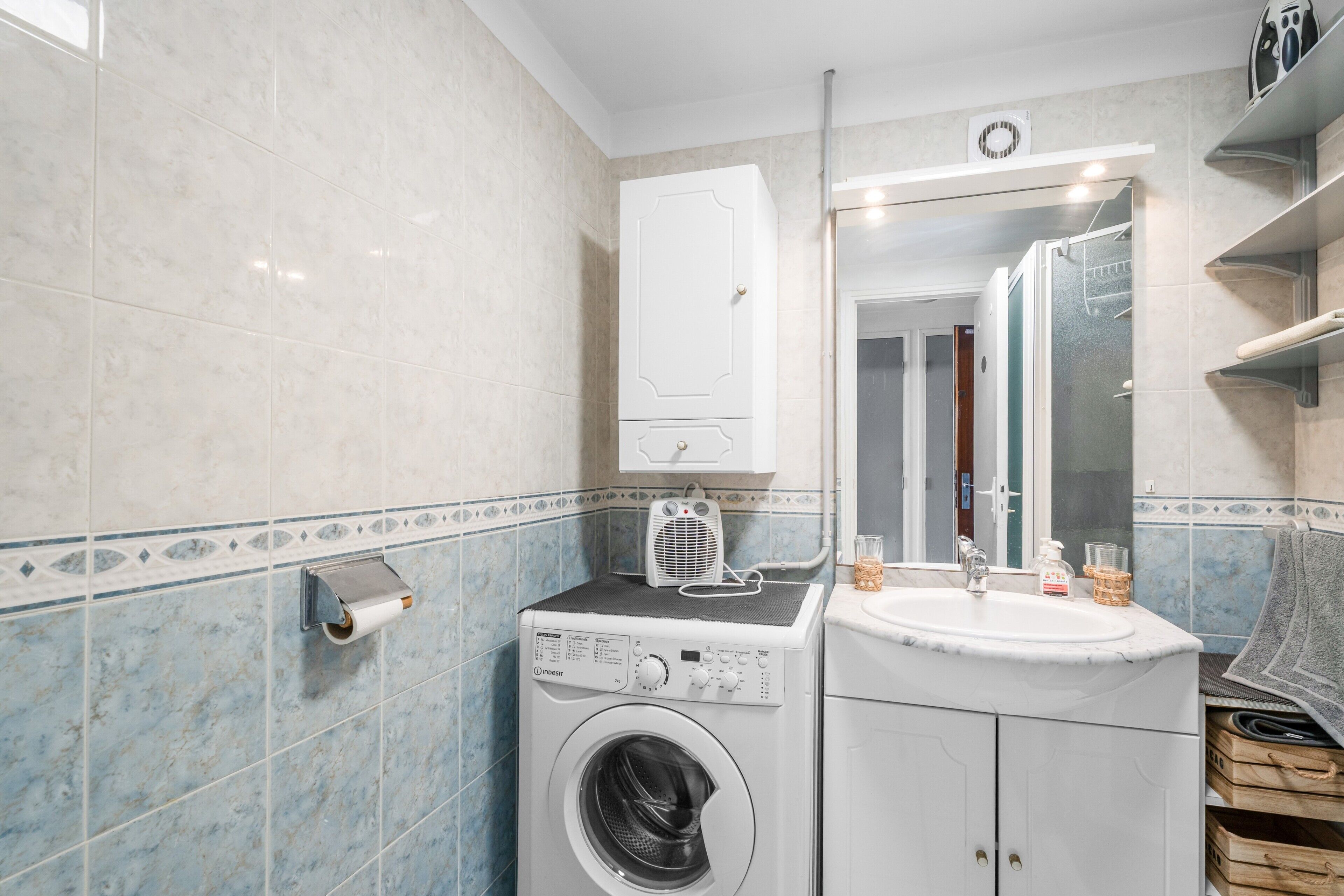A compact bathroom with a washing machine, a sink, and a mirror.