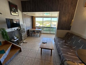 A living room with a TV, a fan, a table, and a sofa. - T2 Apartment 5 Minutes from the Beach with Wi-Fi and Air Conditioning (Six-Fours-les-Plages)