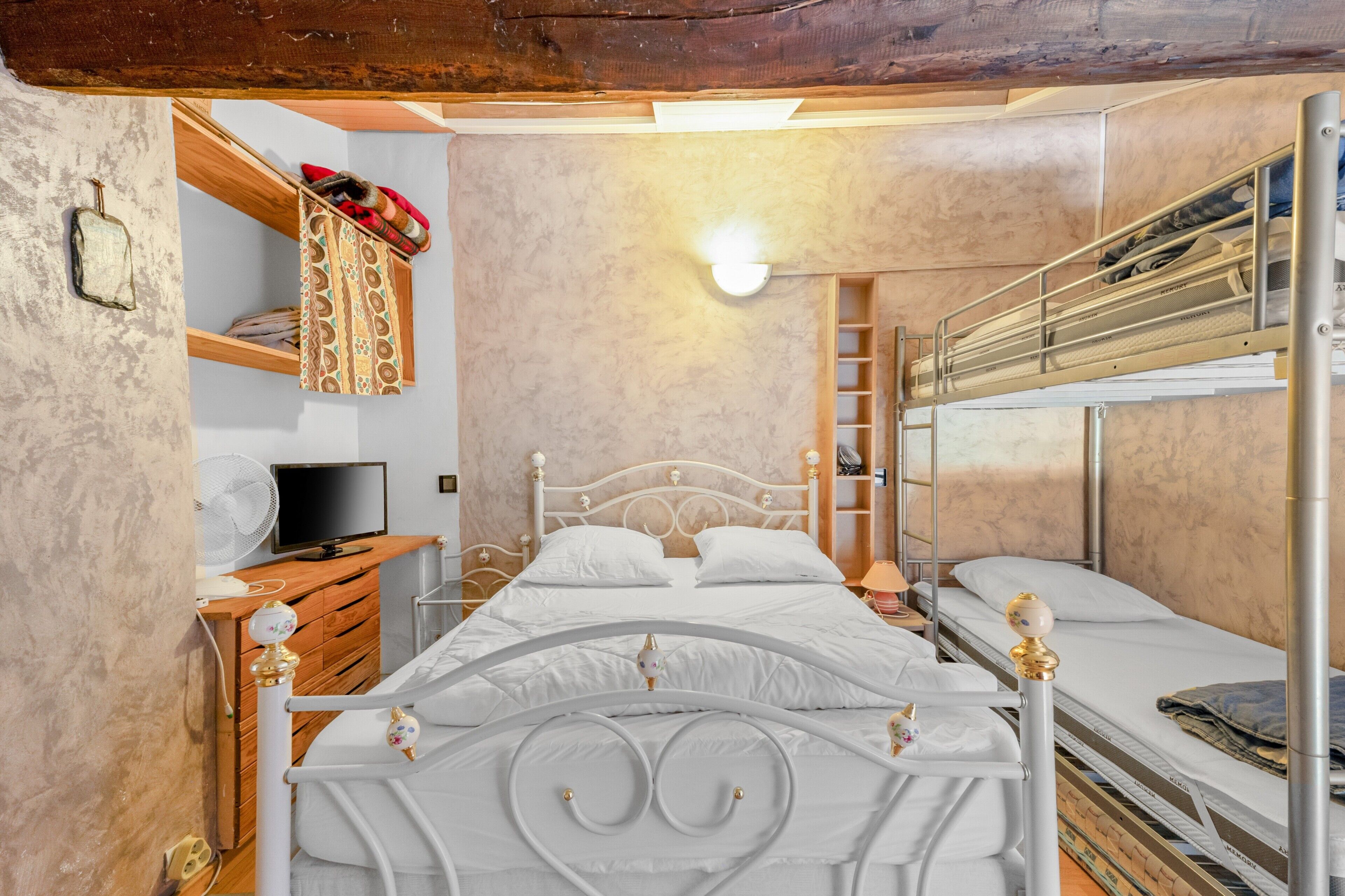 A bunk bed with a TV on a wooden dresser, a fan, and a light fixture.