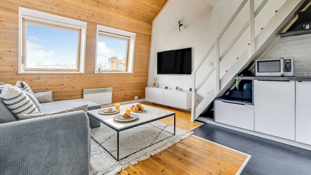 A modern living room with a sofa, coffee table, and a TV. There is a kitchen area with a microwave and cabinets. - 3P duplex on the outskirts of Paris (Le Kremlin-Bicêtre)
