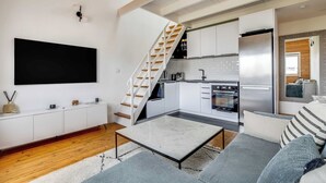 A modern living room with a flat-screen TV, a sofa, a coffee table, and a staircase leading to a kitchen. - 3P duplex on the outskirts of Paris (Le Kremlin-Bicêtre)