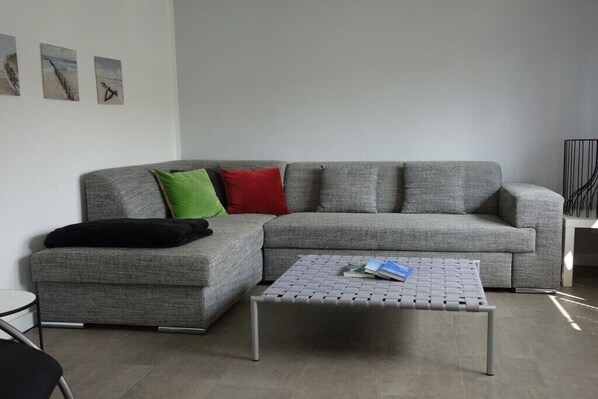 A modern living room with a grey sectional sofa, a small round coffee table, and a black chair. - Holiday home with 3 bedrooms (Ostseebad Binz)