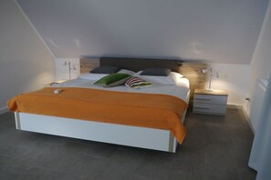 Ein modernes Schlafzimmer mit einem weißen Bett, einer orangefarbenen Tagesdecke und einem hölzernen Kopfteil.