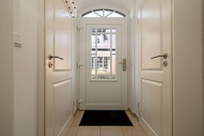 A white door with a glass panel, a black doormat, and a tiled floor. - Holiday home in Hörnum with swimming pool (Hörnum)