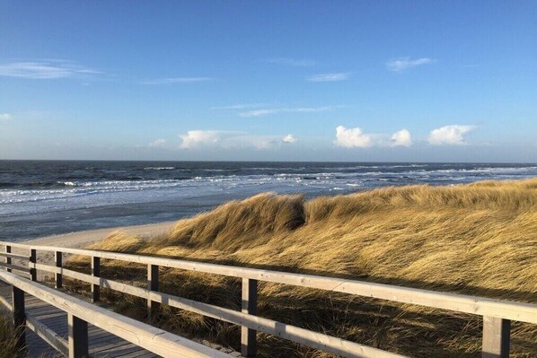 A wooden boardwalk leading to a beach with dunes and the ocean in the background. - Holiday home in Hörnum with swimming pool (Hörnum)
