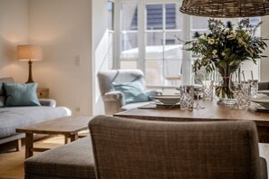A dining area with a table set for four, a wicker chair, and a vase with flowers. - Holiday home in Hörnum with swimming pool (Hörnum)