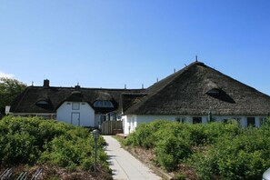 Ein traditionelles Haus mit Strohdach, einem Weg zum Eingang und umgebender Bepflanzung.