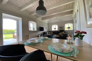 Ein Essbereich mit einem Tisch für vier Personen, eine Couch im Hintergrund und Blick ins Freie.