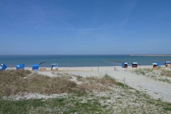 A beach with a clear sky, a sandy path, and several beach huts.