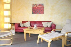 Ein rotes Ledersofa mit weißen Kissen, ein Holztisch und zwei Holzsesseln ebenfalls mit weißen Kissen.