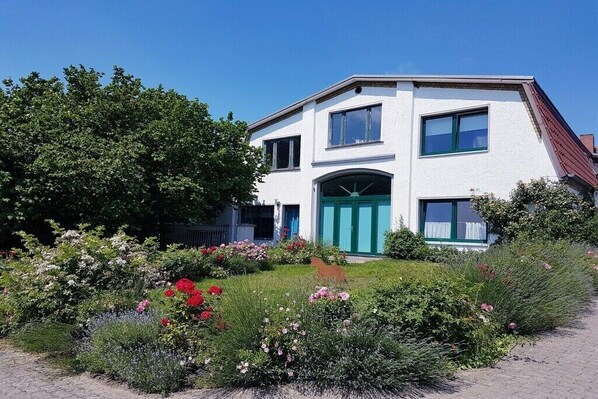 A two-story house with a white exterior, a green door, and a garden with various plants and flowers. - Holiday apartment with 2 bedrooms (Waldeck)