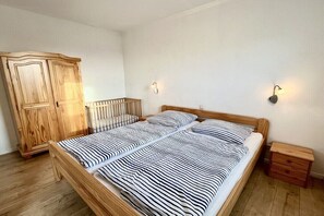 A bedroom with a wooden bed, a wooden wardrobe, and two wall-mounted light fixtures. - Holiday apartment with 2 bedrooms (Waldeck)