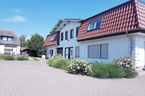 Ein Wohngebäude mit befestigter Auffahrt, einer Haustür und einem kleinen Garten mit rosa Blumen.