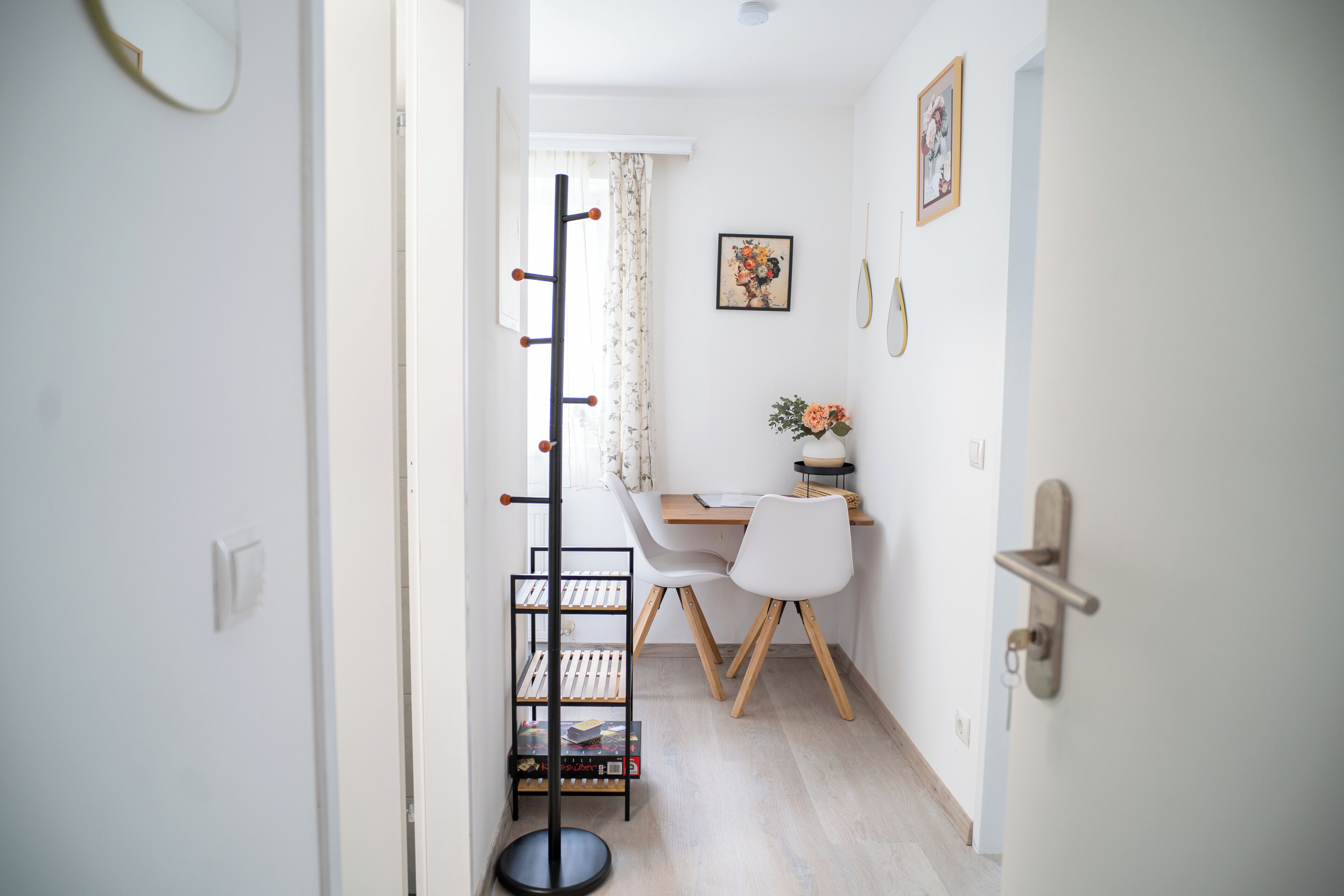 Un pasillo que conduce a un comedor con una mesa, sillas, un perchero y una puerta con una llave en la cerradura.