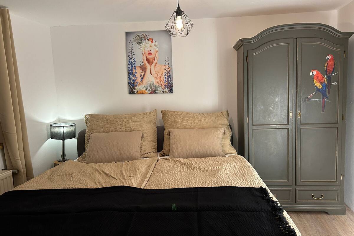A bedroom with a bed, a lamp, a wardrobe, and a painting on the wall.