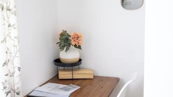Un comedor con una mesa de madera, sillas blancas, un florero con flores y dos espejos colgantes.