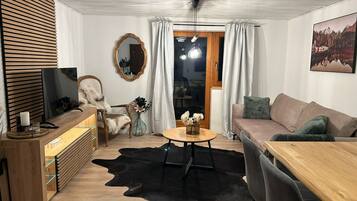 A modern living room with a wooden TV stand, a leather sofa, a dining table, and a black leather rug.