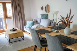 A modern living room with a sofa, dining table, chairs, a coffee table, and a vase with plants.