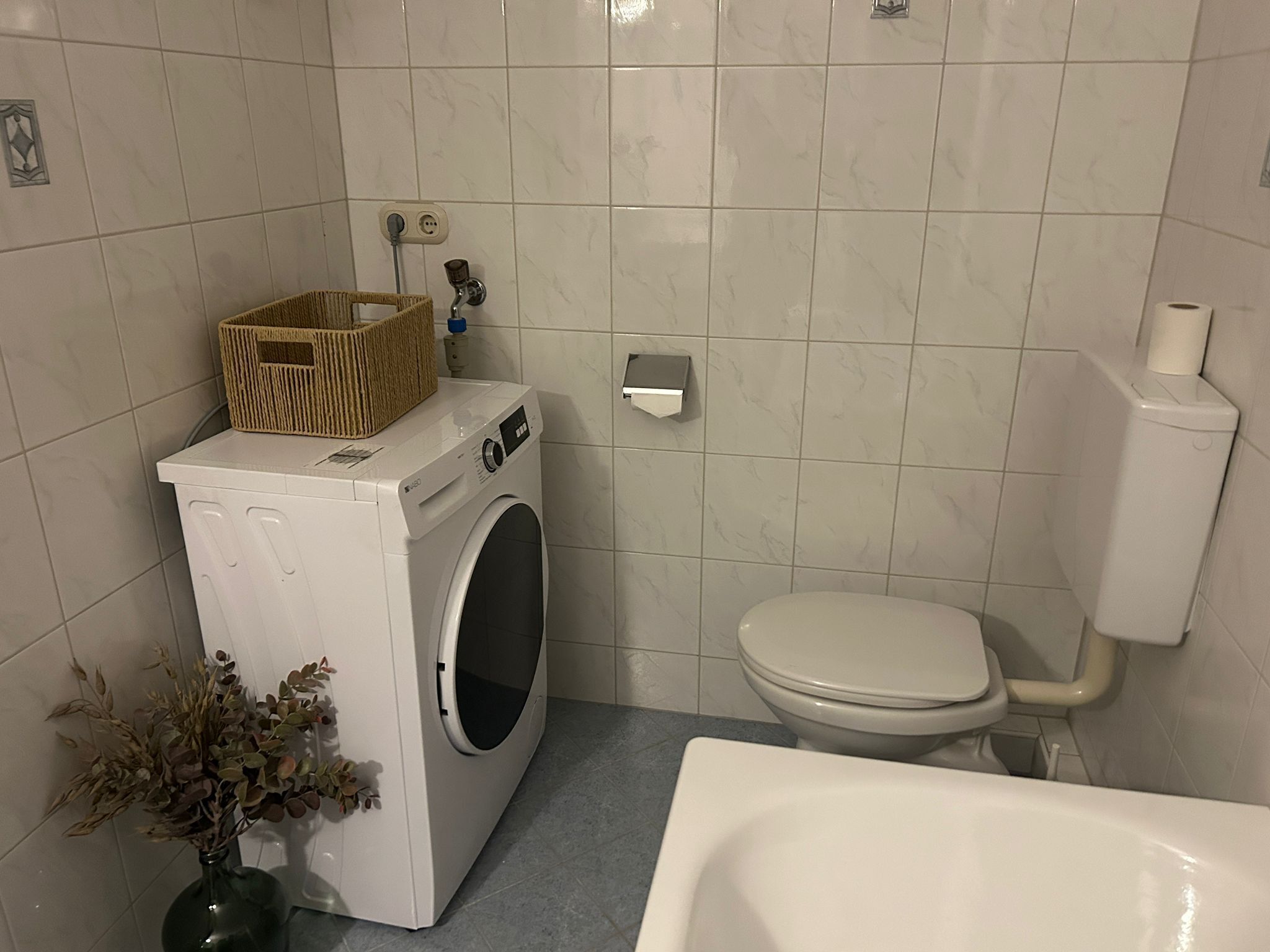 A compact bathroom with a washing machine, toilet, and a bathtub.