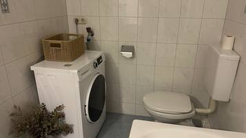 A compact bathroom with a washing machine, toilet, and a bathtub.