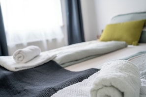 A neatly made bed with rolled towels, a grey blanket, and a yellow pillow.