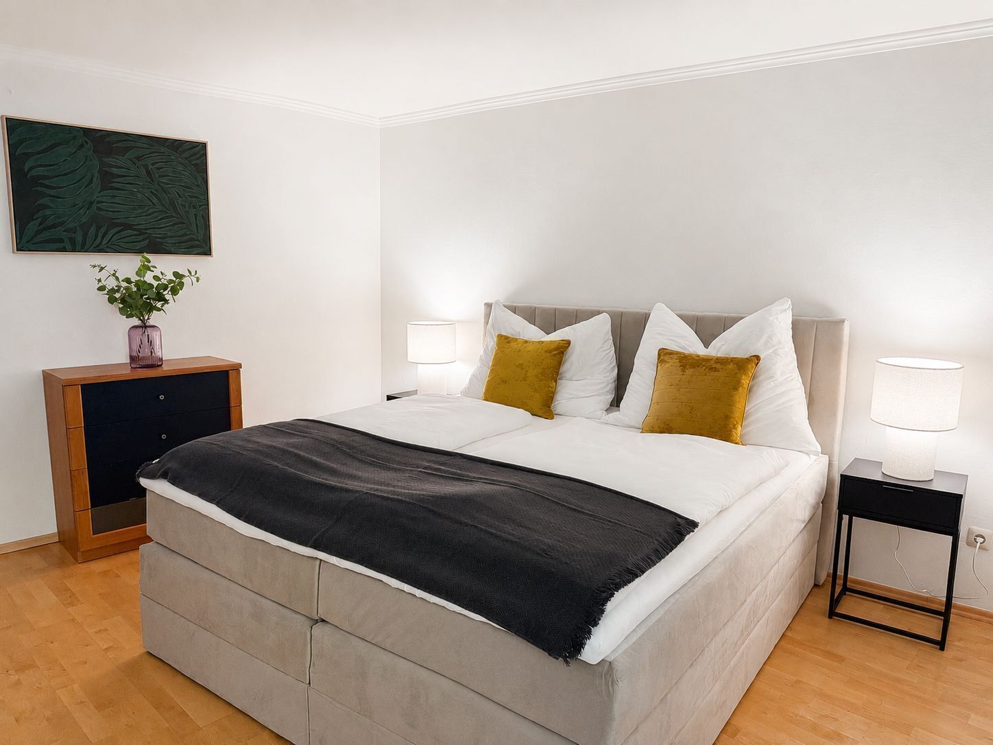 A neatly made bed with a grey headboard, white bedding, and two mustard-colored pillows.