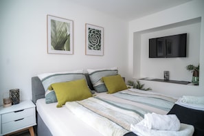 A modern bedroom with a bed, pillows, a nightstand, a TV, and framed botanical artwork on the wall.