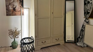 A room with a large wardrobe, a mirror, a vase with dried flowers, and a black woven basket.