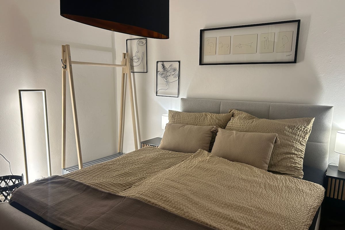 A neatly arranged bedroom with a bed, a bedside table, a lamp, and framed artwork on the wall.