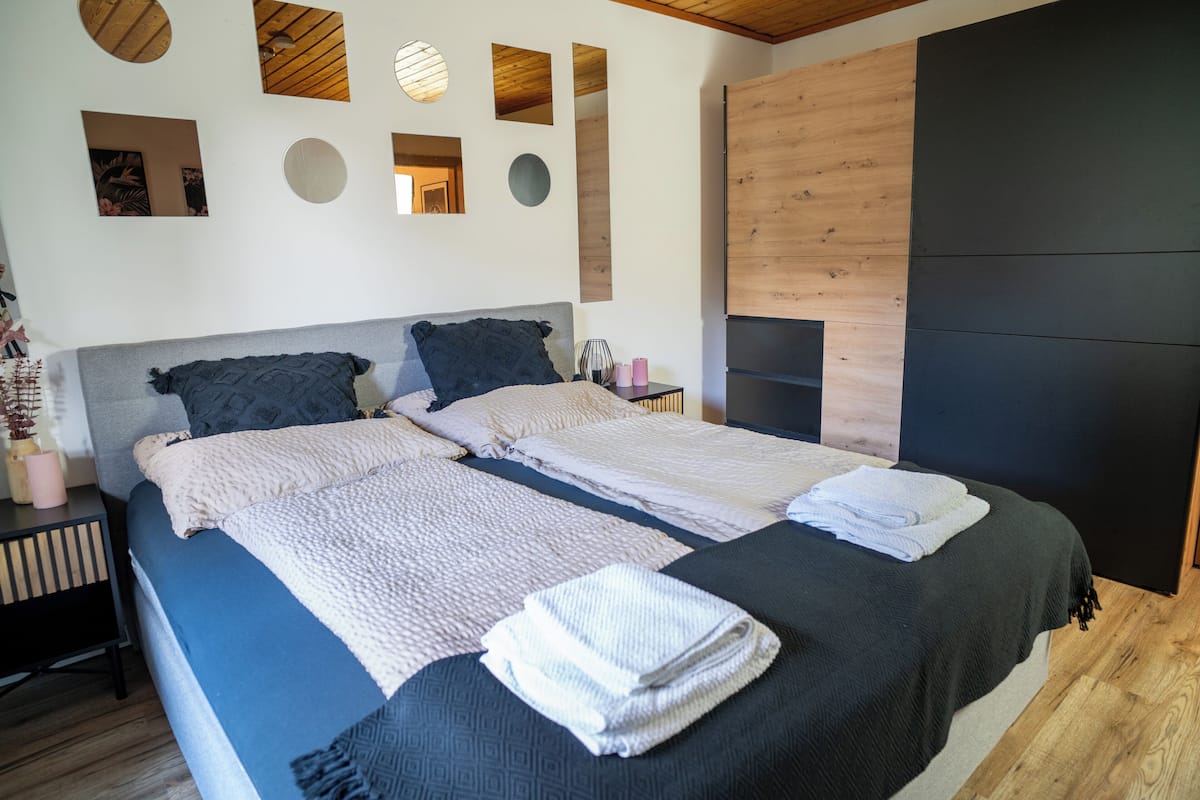 A double bed with two pillows, a bedside table with a lamp, and a mirror on the wall.