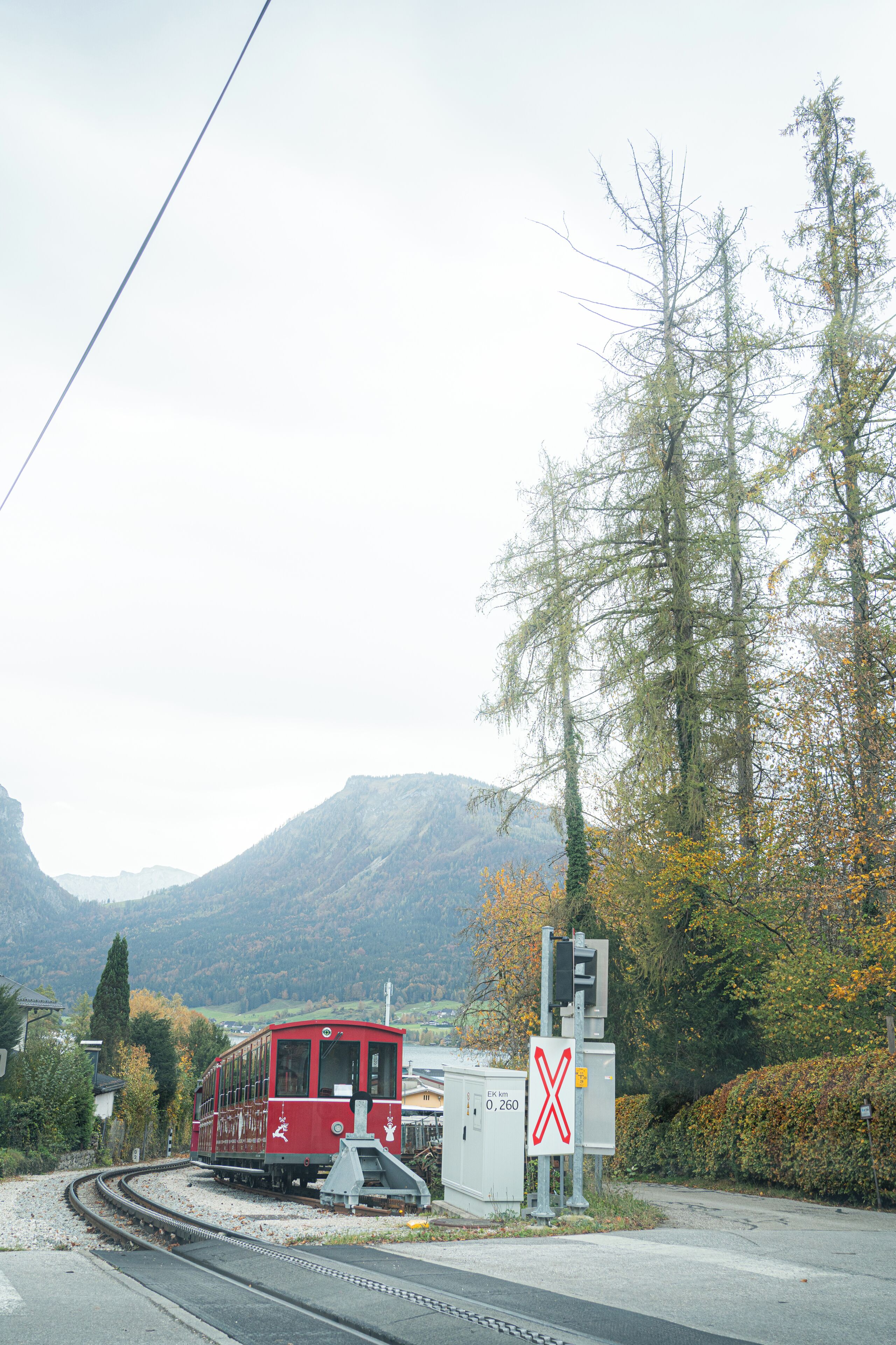 A red train on tracks, a railway crossing sign, and a mountainous landscape.
