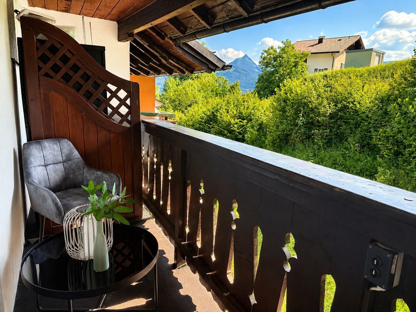Ein Balkon mit Holzgeländer, einem Stuhl und einem Tisch mit einer Pflanze.